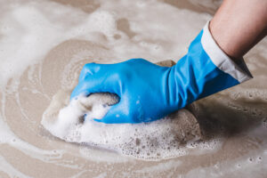 Hand of man wearing blue rubber gloves is using a sponge cleaning the tile floor.